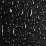 Macro shot of water droplets on a black surface, showcasing texture and detail.